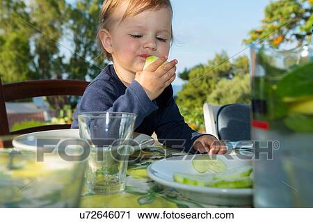 Stock Image - Female toddler eating at table outdoors. Fotosearch