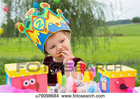 Picture - Female toddler eating birthday cake in garden. Fotosearch
