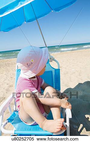 Stock Photography - Female toddler looking over her shoulder at sea from beach chair. Fotosearch