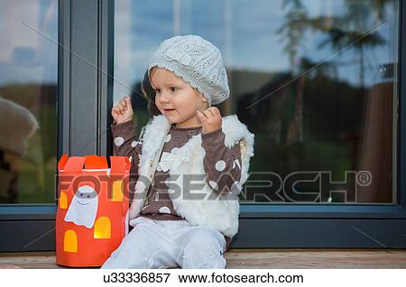 Stock Photo - Female toddler sitting on windowsill with home made halloween lantern. Fotosearch