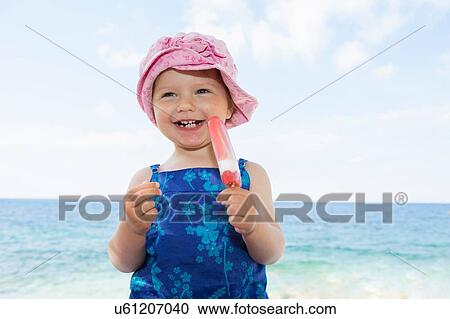 Female toddler wearing sunhat eating ice lolly on beach View Large Photo Image Stock Image - Female toddler wearing sunhat eating ice lolly on beach. Fotosearch
