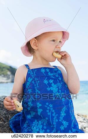 Female toddler wearing sunhat eating doughnut on beach View Large Photo Image Stock Photo - Female toddler wearing sunhat eating doughnut on beach. Fotosearch