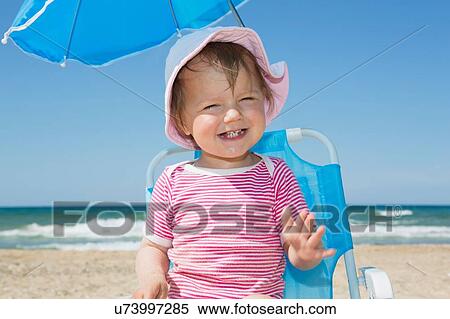 Stock Photography - Female toddler wearing sunhat on beach chair. Fotosearch