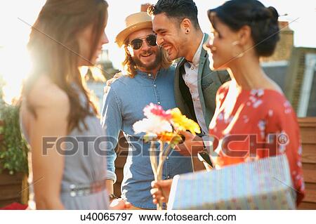 Friends at party on roof terrace holding flowers and gift smiling View Large Photo Image Stock Photo - Friends at party on roof terrace holding flowers and gift smiling. Fotosearch