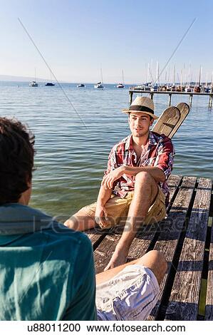 Friends sitting face to face on wood pier next to lake, Schondorf, Ammersee, Bavaria, Germany View Large Photo Image Stock Image - Friends sitting face to face on wood pier next to lake, Schondorf, Ammersee, Bavaria, Germany. Fotosearch