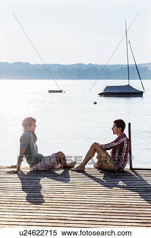 Friends sitting face to face on wood pier next to lake, Schondorf, Ammersee, Bavaria, Germany View Large Photo Image Stock Photography - Friends sitting face to face on wood pier next to lake, Schondorf, Ammersee, Bavaria, Germany. Fotosearch