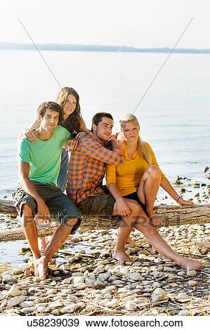 Friends sitting on driftwood next to shoreline looking at camera smiling, Schondorf, Ammersee, Bavaria, Germany View Large Photo Image Stock Photo - Friends sitting on driftwood next to shoreline looking at camera smiling, Schondorf, Ammersee, Bavaria, Germany. Fotosearch