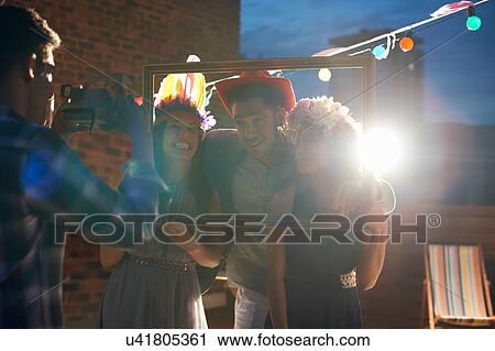 Stock Image - Friends taking photograph at early evening party. Fotosearch