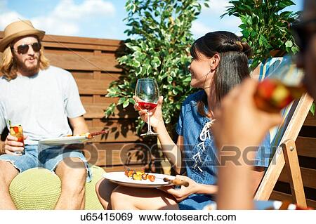 Stock Photo - Friends talking and drinking at rooftop party. Fotosearch