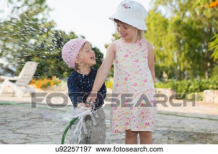 Girl and toddler sister playing with water hosepipe in garden View Large Photo Image Stock Photo - Girl and toddler sister playing with water hosepipe in garden. Fotosearch
