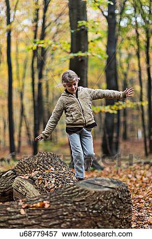 Stock Photo - Girl balancing on tree trunk in autumn forest. Fotosearch