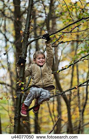 Stock Image - Girl hanging on to tree branch in autumn forest. Fotosearch