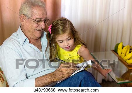 Stock Photo - Girl looking at grandfather writing in notebook. Fotosearch