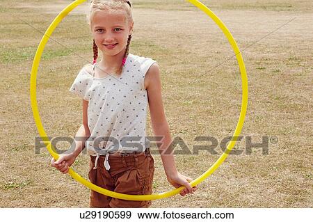 Stock Photo - Girl looking through hula hoop smiling at camera. Fotosearch