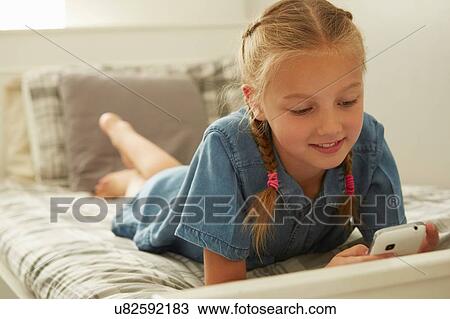 Girl lying on bed looking down at smartphone smilinhg View Large Photo Image Stock Image - Girl lying on bed looking down at smartphone smilinhg. Fotosearch