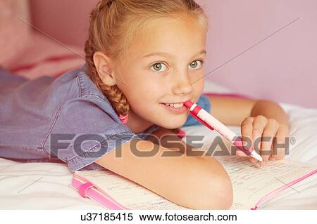 Girl on bed writing in notebook, holding pen looking away smiling View Large Photo Image Stock Photography - Girl on bed writing in notebook, holding pen looking away smiling. Fotosearch