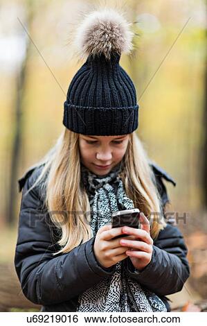 Stock Photograph - Girl using smartphone in autumn forest. Fotosearch