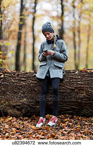 Girl using smartphone on tree trunk in autumn forest View Large Photo Image Stock Image - Girl using smartphone on tree trunk in autumn forest. Fotosearch