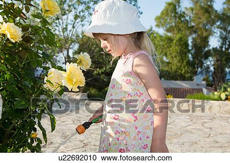 Stock Image - Girl wearing sunhat watering roses. Fotosearch