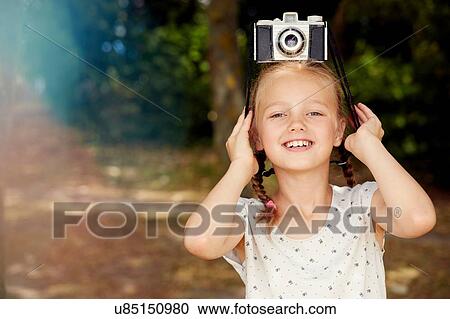 Stock Image - Girl with film camera on head looking at camera smiling. Fotosearch