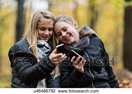 Stock Image - Girls using smartphone in autumn forest. Fotosearch