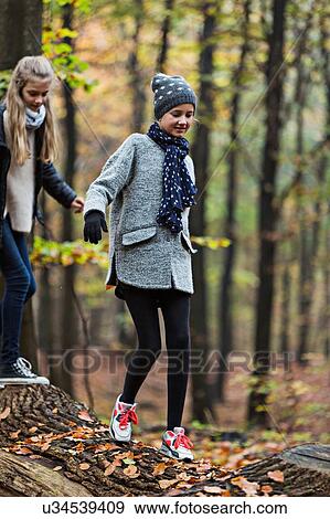 Stock Photo - Girls walking on tree trunk in autumn forest. Fotosearch