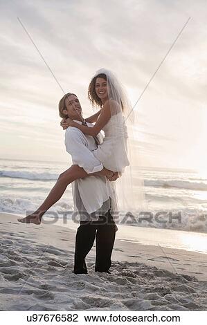 Groom carrying bride on beach View Large Photo Image Stock Image - Groom carrying bride on beach. Fotosearch