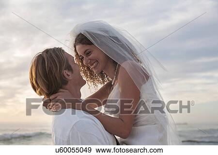 Groom carrying bride on beach View Large Photo Image Stock Photo - Groom carrying bride on beach. Fotosearch