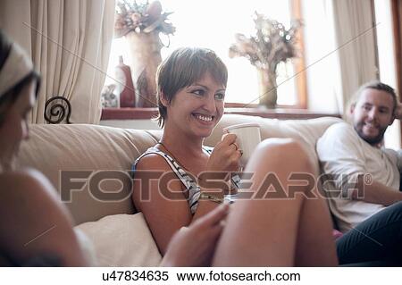 Stock Photography - Group of friends, sitting on sofa, drinking tea. Fotosearch