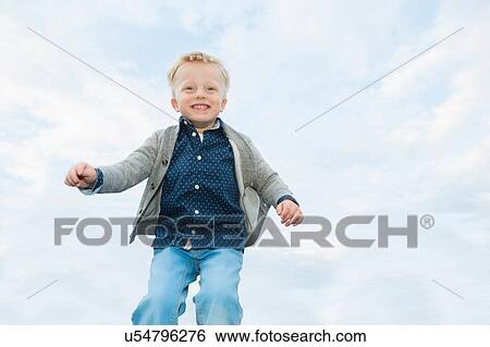Stock Photograph - Happy boy mid air against sky. Fotosearch