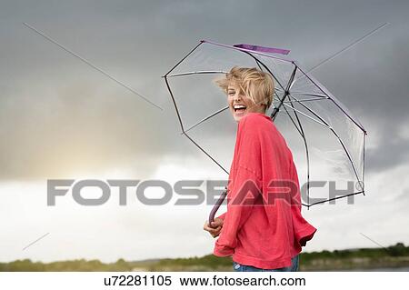 Stock Photography - Happy young woman holding transparent umbrella under storm clouds. Fotosearch