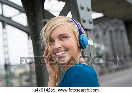 Happy young woman wearing headphones on bridge looking over her shoulder View Large Photo Image Stock Photography - Happy young woman wearing headphones on bridge looking over her shoulder. Fotosearch
