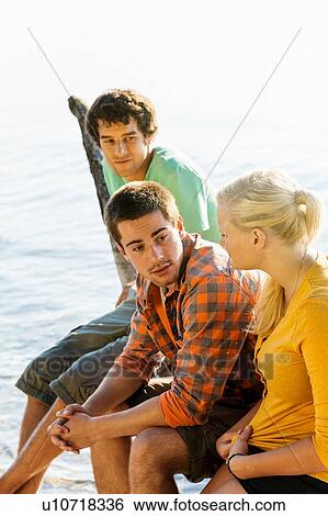 Stock Photograph - High angle side view of friends sitting next to water chatting. Fotosearch