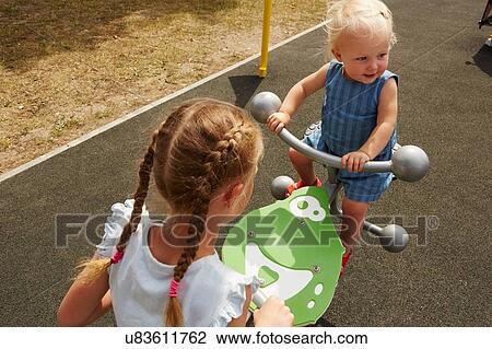Stock Image - High angle view of sisters sitting on seesaw. Fotosearch