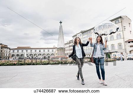 Stock Photo - Lesbian couple holding umbrella fooling around holding hands smiling, Piazza Santa Maria Novella, Florence, Tuscany, Italy. Fotosearch