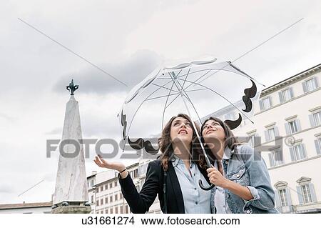 Lesbian couple holding umbrella checking for rain with hand, looking up, Piazza Santa Maria Novella, Florence, Tuscany, Italy View Large Photo Image Picture - Lesbian couple holding umbrella checking for rain with hand, looking up, Piazza Santa Maria Novella, Florence, Tuscany, Italy. Fotosearch