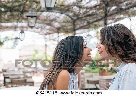 Stock Photo - Lesbian couple in plant covered archway face to face smiling, Florence, Tuscany, Italy. Fotosearch
