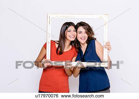 Stock Photograph - Lesbian couple looking through picture frame at camera smiling. Fotosearch