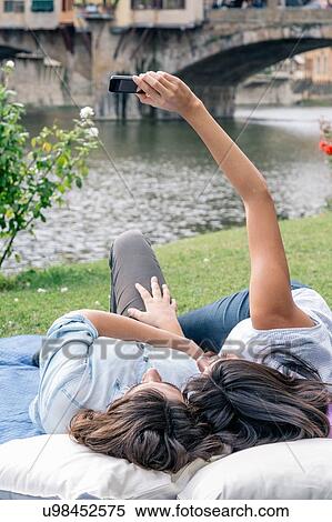 Stock Photography - Lesbian couple lying down using smartphone to take selfie in front of Ponte Vecchio over river Arno, Florence, Tuscany, Italy. Fotosearch