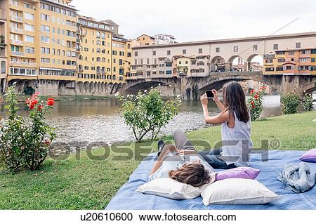 Stock Image - Lesbian couple on blanket using digital camera to photograph Ponte Vecchio over river Arno, Florence, Tuscany, Italy. Fotosearch