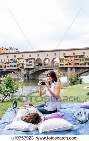 Lesbian couple on blanket using smartphone to take photograph in front of Ponte Vecchio and river Arno, Florence, Tuscany, Italy View Large Photo Image Stock Image - Lesbian couple on blanket using smartphone to take photograph in front of Ponte Vecchio and river Arno, Florence, Tuscany, Italy. Fotosearch