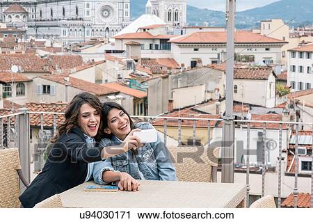 Lesbian couple sitting at table on roof terrace using smartphone to take selfie smiling, Florence, Tuscany, Italy View Large Photo Image Stock Image - Lesbian couple sitting at table on roof terrace using smartphone to take selfie smiling, Florence, Tuscany, Italy. Fotosearch