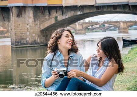 Lesbian couple sitting together looking at digital camera laughing, in front of Ponte Vecchio, Florence, Tuscany, Italy View Large Photo Image Stock Photograph - Lesbian couple sitting together looking at digital camera laughing, in front of Ponte Vecchio, Florence, Tuscany, Italy. Fotosearch