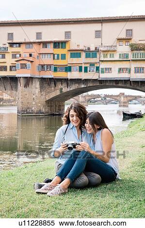 Stock Photography - Lesbian couple sitting together looking at digital camera in front of Ponte Vecchio smiling, Florence, Tuscany, Italy. Fotosearch