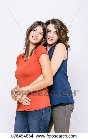 Picture - Lesbian couple standing hugging looking at camera smiling. Fotosearch