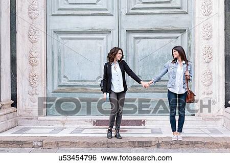 Stock Photograph - Lesbian couple standing in oversized church doorway holding hands, Piazza Santa Maria Novella, Florence, Tuscany, Italy. Fotosearch