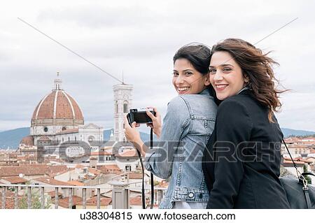 Stock Photography - Lesbian couple taking photo of Florence Cathedral and Giotto's Campanile looking over shoulder smiling, Florence, Tuscany, Italy. Fotosearch