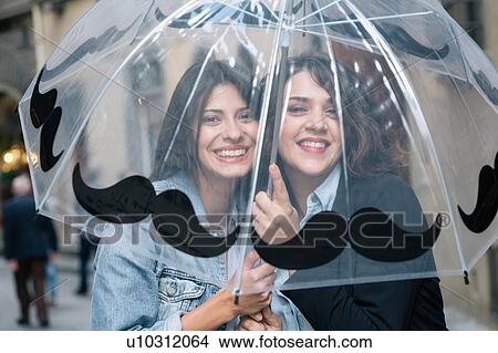 Picture - Lesbian couple underneath transparent umbrella looking at camera smiling, Florence, Tuscany, Italy. Fotosearch