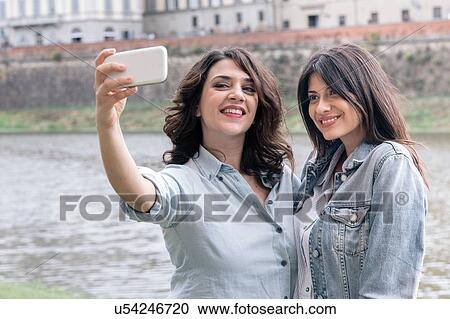 Lesbian couple using smartphone to take selfie next to Arno river, Florence, Tuscany, Italy View Large Photo Image Stock Image - Lesbian couple using smartphone to take selfie next to Arno river, Florence, Tuscany, Italy. Fotosearch