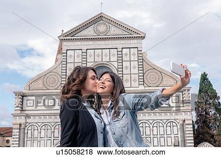 Lesbian couple using smartphone to take selfie in front of church, kiss on cheek, Piazza Santa Maria Novella, Florence, Tuscany, Italy View Large Photo Image Stock Photo - Lesbian couple using smartphone to take selfie in front of church, kiss on cheek, Piazza Santa Maria Novella, Florence, Tuscany, Italy. Fotosearch